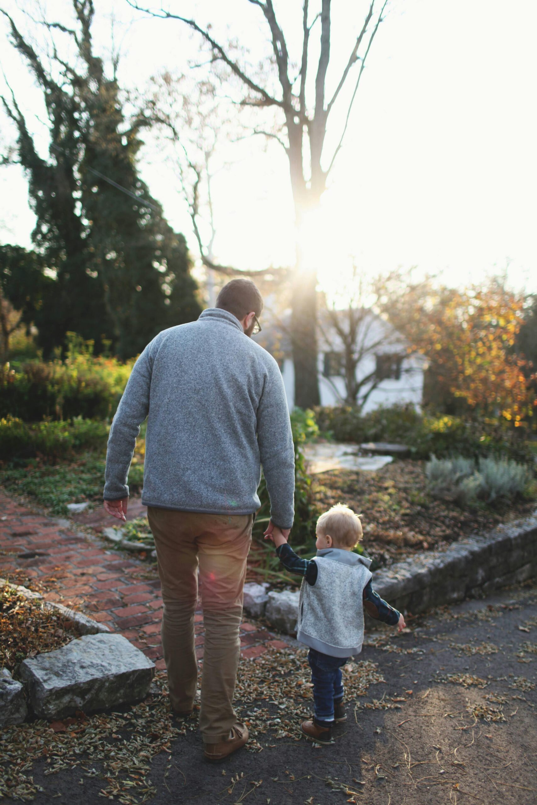 A heartwarming scene of a father and son walking hand in hand at sunset in a park.