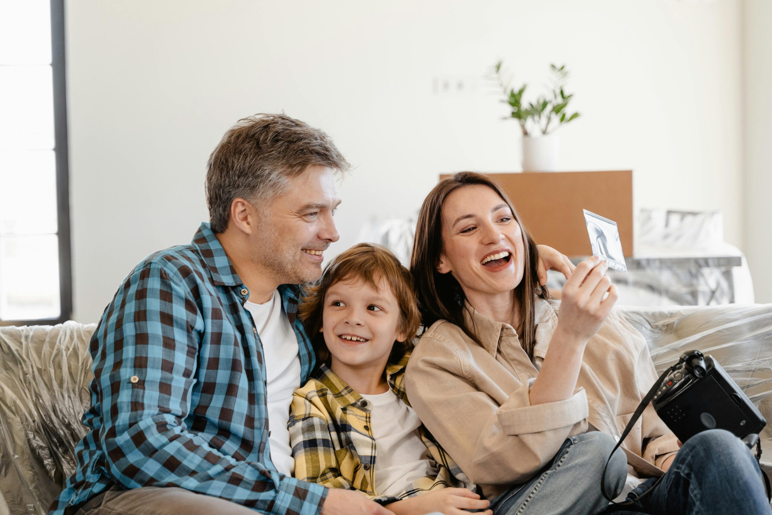 A cheerful family enjoys time together on a couch surrounded by moving boxes in their new home.